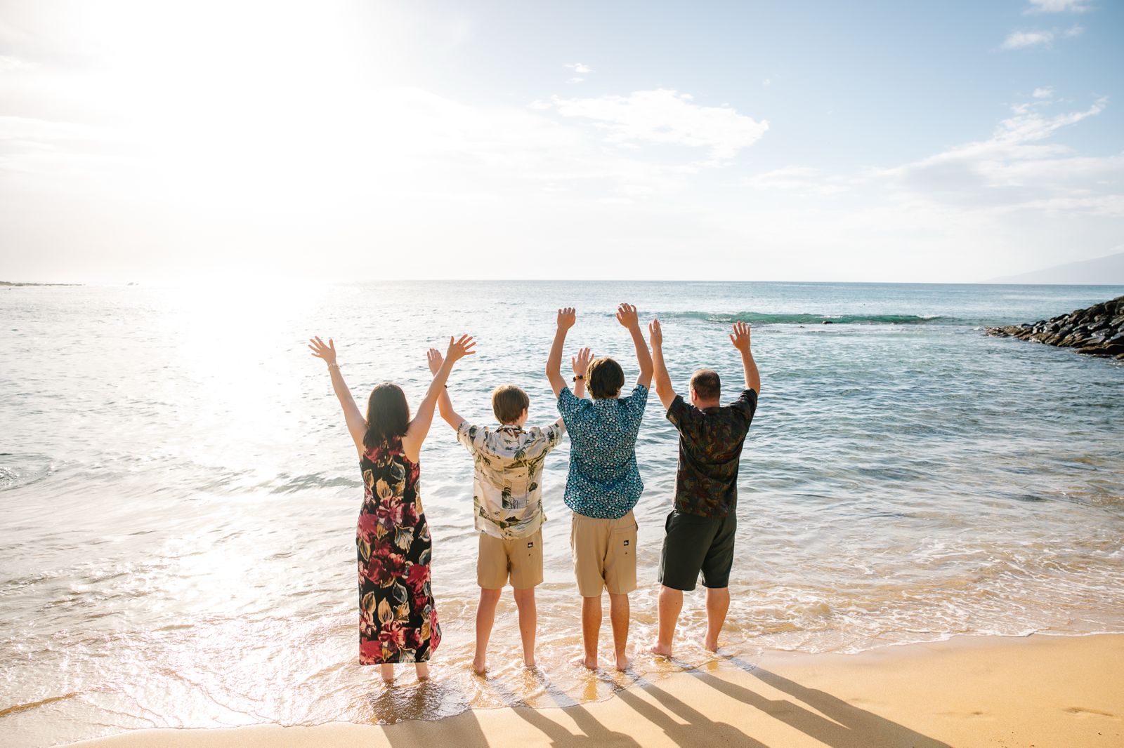 Family raising hands toward the ocean at sunrise